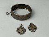 deux bijoux en argent posés sur une surface blanche, entourés d'une chaîne