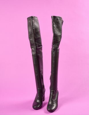 une paire de bottes en cuir noir sur fond rose
