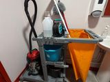 un chariot de nettoyage dans un coin des toilettes, sur lequel se trouvent une serpillière et un seau