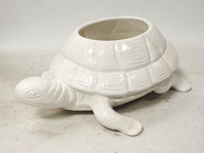 une petite jardinière en forme de tortue blanche posée par terre
