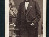 portrait d'un homme en costume et nœud papillon, debout devant une table