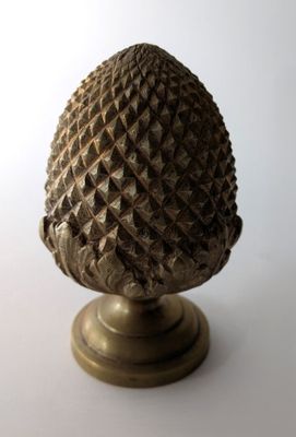 une petite pomme de pin posée sur un socle, sur une surface blanche