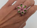 la main tient une bague en forme de fleur rose et verte