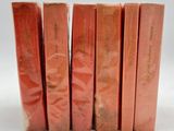 six livres rouges sont alignés sur une surface blanche