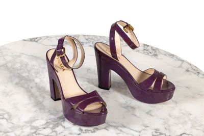 des sandales à talons hauts violettes posées sur une table en marbre, sur fond blanc