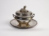 an antique silver plate with a lid and a saucer on a saucer