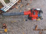 a red leaf blower sitting on the ground next to a fence