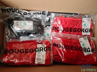 trois t-shirts rouges sont emballés dans des sacs en plastique posés sur une boîte en carton