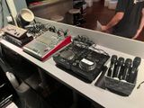 un homme debout devant une table sur laquelle sont posés de nombreux appareils électroniques