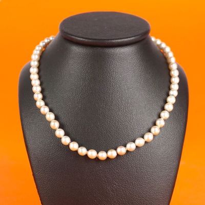 a white pearl necklace on a black mannequin with orange background