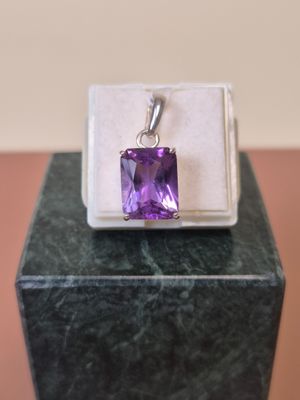 une photo d'un pendentif en pierre violette posé sur une boîte blanche