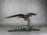 sculpture en bronze représentant un oiseau sur une vague, sur fond gris