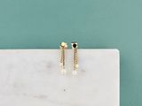 une paire de boucles d'oreilles en or ornées de perles, posées sur une surface en marbre