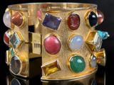 gold cuff bracelet with multi colored stones on a black surface