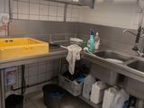 a kitchen with a sink, counter, and shelves with cleaning supplies