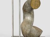 sculpture of a curved metal object with a gold disc on a marble base