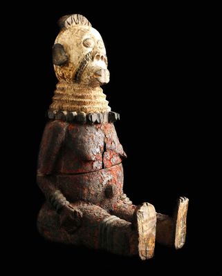 une vieille statue en bois représentant un homme assis sur une surface noire
