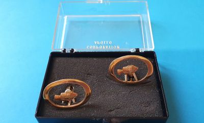une paire de bracelets manchette dorés, présentés dans un coffret noir posé sur un fond bleu