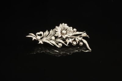 une broche en argent ornée de fleurs et de feuilles sur un fond noir