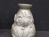 a silver vase with a flower on it on a black surface