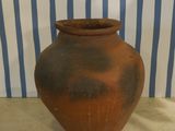 a brown vase sitting on a table in front of a blue and white striped wall