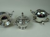 two silver teapots and a sugar bowl on a white surface