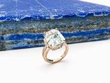 un gros plan d'une bague en diamant posée sur un rocher, avec une pierre bleue en arrière-plan