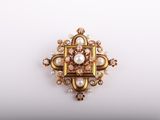 a close up of a gold and pearl broochle on a white surface