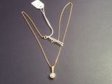 two gold necklaces with a white diamond on a black surface