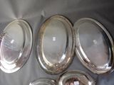 six silver oval serving trays on a table with a woman in the background