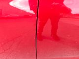 a man standing in front of a red car with his reflection on the door