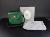 Le petit sac à main vert se trouve à côté d'une boîte blanche et d'un tissu blanc.