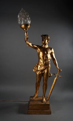 LAMPE en tôle dorée formée d'un porteur de flambeau, le feu …