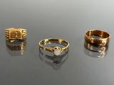 three gold rings and a ring with a pearl on top of a table