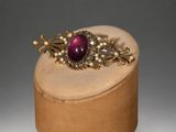 an image of a broochle with pearls on a wooden stand