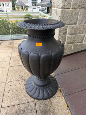 un vase noir posé sur le trottoir, à côté d'un mur de briques