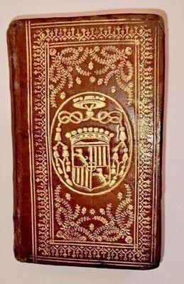 an old book with a gold and red cover sitting on a white surface