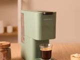 une cafetière verte posée sur une table, à côté d'une tasse de café