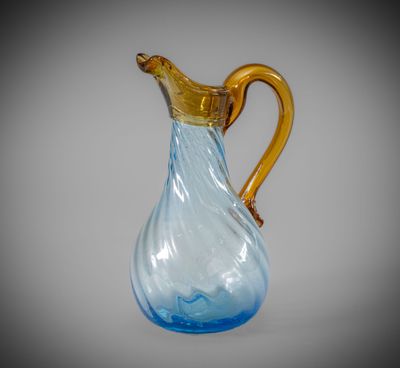 a blue glass pitcher with a gold handle on a gray background