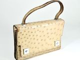 beige ostrich leather handbag with metal handles on a white surface