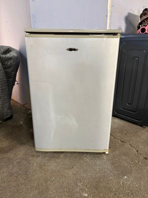 un petit réfrigérateur blanc dans le coin d'une pièce