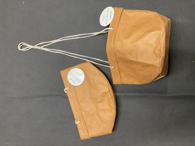 deux sacs en papier kraft avec des étiquettes accrochées dessus, posés sur une surface noire
