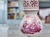 a pink and white vase sitting on a table in front of a bookshelf