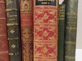 several old books are lined up on a shelf in front of a white wall
