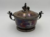 an antique silverplated bowl with a lid and two figurines on it