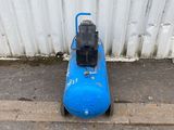 a blue air compressor sitting on the ground next to a white wall