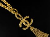 a gold necklace with a chain and a tassel on a black background