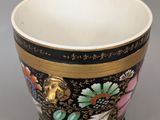 un gros plan d'une tasse noire et dorée ornée de fleurs