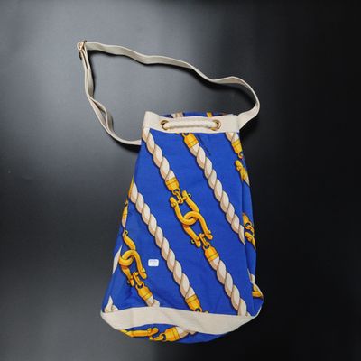 un sac à main bleu et jaune muni d'une anse en corde, sur un fond noir