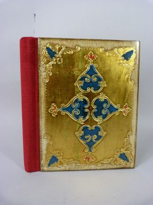 un livre doré à la couverture bleue et rouge posé sur une surface blanche
